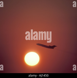 commercial jet flying silhouetted against setting sun Stock Photo