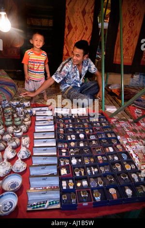 Man & his son with counterfeit products, fake knockoff goods knock off watch / watches, & Mont Blanc pen / pens. Night market in Luang Prabang. Laos. Stock Photo