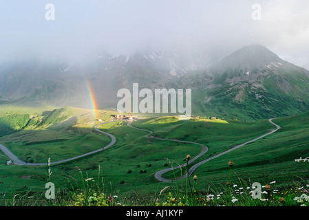 France, Hautes Alpes, Lautaret Pass on July between two showers, rainbow and road rising to the Galibier Pass to the right Stock Photo