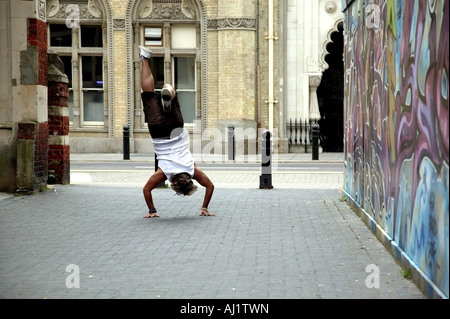 Man in summer attire doing a handstand next to a graffiti wall Stock Photo
