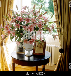 China vase full of blossoming lilies on circular table in window alcove Stock Photo