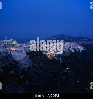 Cliff top view of clustered white town at dusk with lights and church on edge of cliff at Fira on Santorini The Greek Islands Stock Photo