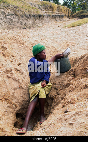 Young woman collecting the last dregs of water from a dry riverbed during a prolonged period of drought. Zimbabwe Stock Photo