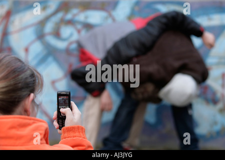 two fighting boys are being filmed by a girl with her mobile phone Stock Photo