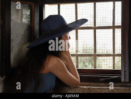 Young woman looking out of a window with a grate with sunlight coming from it Stock Photo