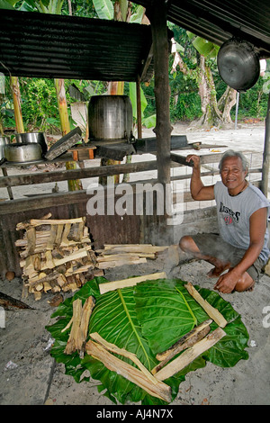 Middle aged local man sits in his kitchen hut by his uhm a traditional pit oven used to cook food Stock Photo