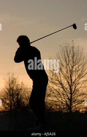 Shilouette of golfer against sunset and trees Stock Photo