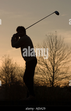 Shilouette of golfer against sunset and trees Stock Photo