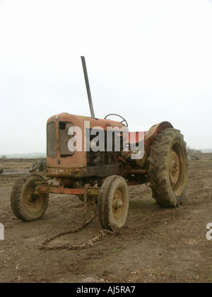 An old red agricultural tractor stands on a field with green grass in ...