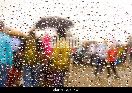 Blurred people seen through raindrops on a transparent umbrella. Stock Photo