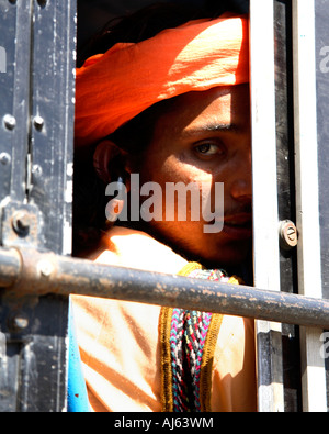 Indian Man wearing saffron coloured shirt and orange turban seated on bus peeking out of window, Junagadh, Saurashtra, India Stock Photo