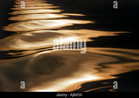 Sunset light reflecting off wave patterns formed by wake of moving boat Stock Photo