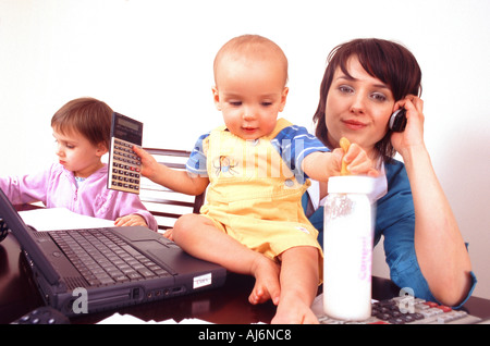 Woman sitting at the desk with her children while talking on the phone and using her laptop. Stock Photo