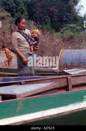 mother and baby with boats beside the mekong river laos. A girl is paddling in the backgroun Stock Photo