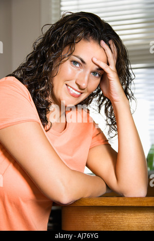 Pretty young adult Caucasian brunette woman sitting with hand on head looking at viewer smiling Stock Photo