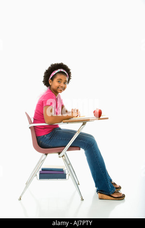 Side view of African American girl sitting in school desk smiling at viewer Stock Photo