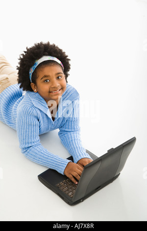 High angle view of African American girl lying on floor using laptop and looking up at viewer Stock Photo