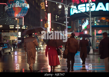 People crossing Broadway carrying umbrellas on rainy night in Times Square New York NY Stock Photo