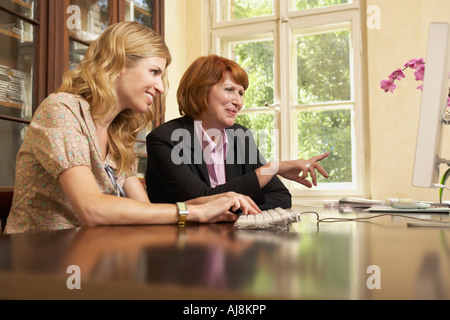 Young woman using computer with middle-aged woman in living room Stock Photo