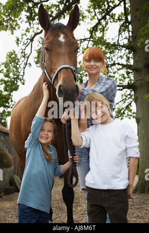 Mother and children (5-6, 7-9) with horse outdoors, portrait