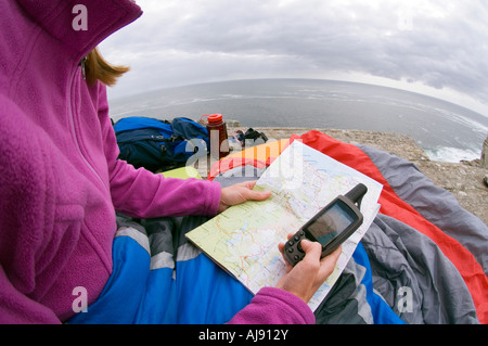 Reading map & GPS at camp on rocky ocean cliff. Stock Photo