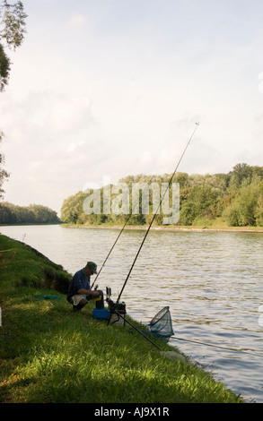 Man fishing on the banks of the Canal du Nord in the Pas de Calais in France Image shows three rods in use with keep net Stock Photo