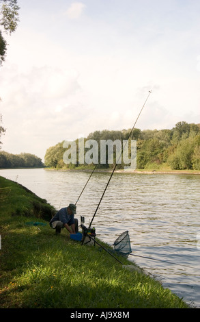 Man fishing on the banks of the Canal du Nord in the Pas de Calais in France Image shows three rods in use with keep net Stock Photo