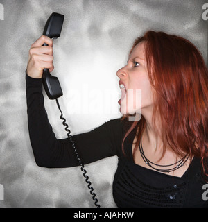 Portrait of pretty young redhead woman holding telephone receiver and yelling Stock Photo
