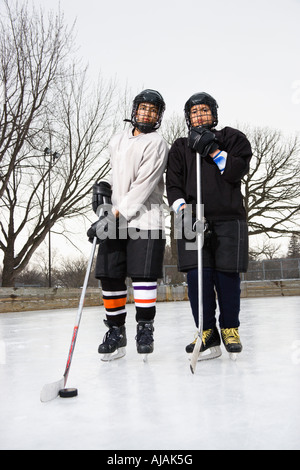 Two boys in ice hockey uniforms holding hockey sticks standing on ice rink in ice skates Stock Photo