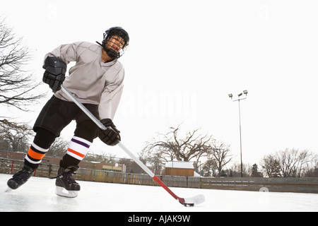 Boy in ice hockey uniform skating on ice rink moving puck Stock Photo