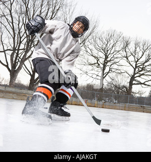 Boy in ice hockey uniform skating on ice rink moving puck Stock Photo