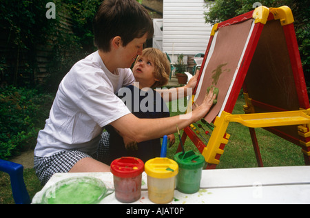 An infant looks into her mother's face while painting art with her mum on an easel in their back garden in South London Stock Photo