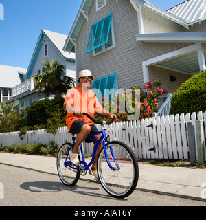 Middle aged African American man bicycling down street next to homes and fence Stock Photo