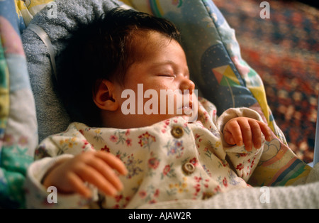 As window light falls over her face a baby girl sleeps soundly in her baby bouncer chair on the living room floor London Stock Photo