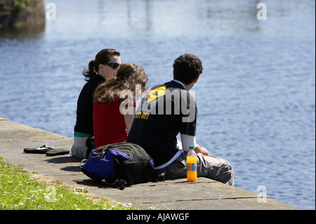 group of three young people enjoying the sunshine on the quay next to the corrib river on a sunday afternoon Stock Photo