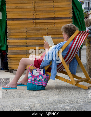 woman sitting back in deck chair reading novel Stock Photo