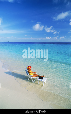 Woman sitting at table with laptop and cellphone on beach in Maldives Stock Photo