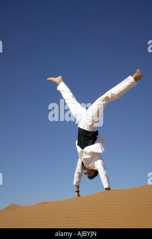 Man in a White Suit Doing a Handstand in the Desert Stock Photo