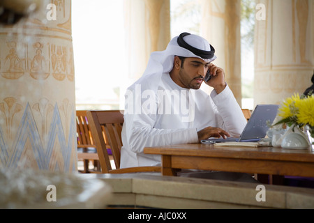 Arab Business Man using Mobile Phone and Computer, sitting on Patio Table in Restaurant Stock Photo