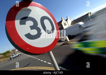 An ambulance races into a 30 mph miles per hour speed limit area marked by a 30 mph warning sign at a road junction. Stock Photo