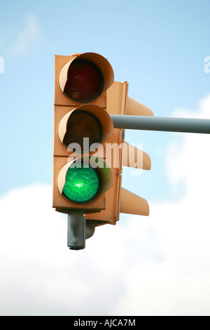 A Overhead traffic light in yellow against a blue clouded sky with the green light lit Stock Photo
