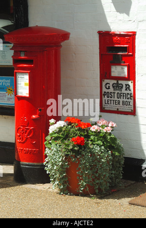 Woolpit village two red GR post boxes outside village post office plants in bloom growing in flower pot on pavement sunny day in Suffolk England UK Stock Photo