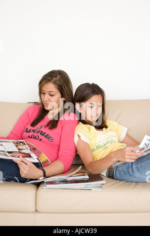 Two Asian Teenage Girls Reading Magazines on Sofa Stock Photo