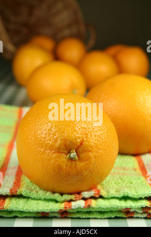 eye level close up view of one orange on a napkin with several out of focus scattered from upturned basket in background Stock Photo