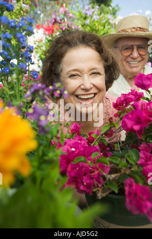 Senior Couple sitting in plant nursery seen through bed of flowers, portrait Stock Photo