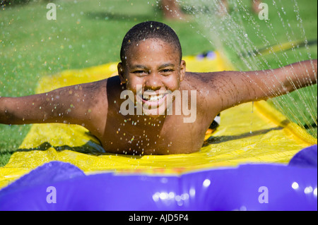 Boy (10-12) Sliding on water slide, front view portrait. Stock Photo