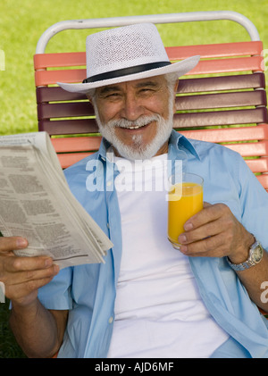 Senior Man sitting on Lawn Chair holding Newspaper and Orange Juice, elevated view portrait. Stock Photo