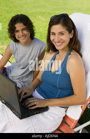 Mother sitting on sunlounger, Using Laptop Outdoors with son (13-15),  portrait. Stock Photo