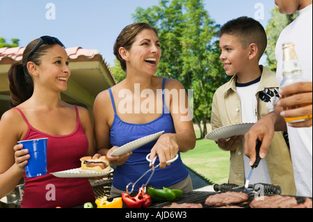 Boy (13-15) with family, gathered around grill at picnic. Stock Photo
