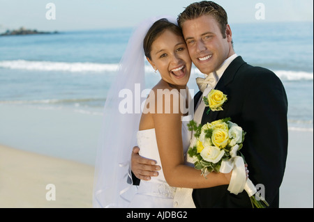 Bride and Groom embracing on beach, (portrait) Stock Photo